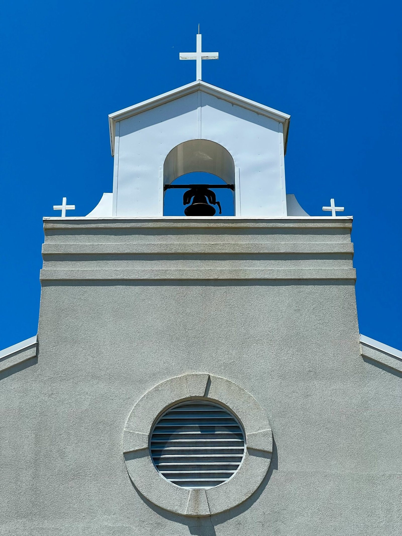 a white building with a bell and a cross on top